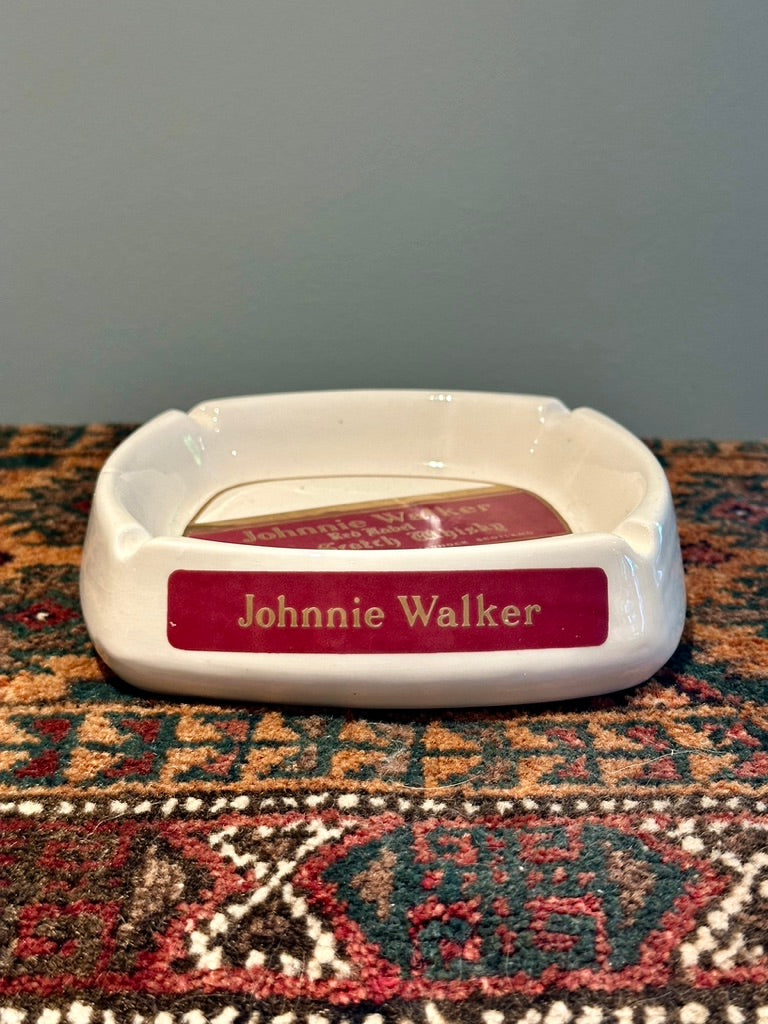 A white ceramic ashtray with a red front plaque reading 'Johnnie Walker' in gold lettering