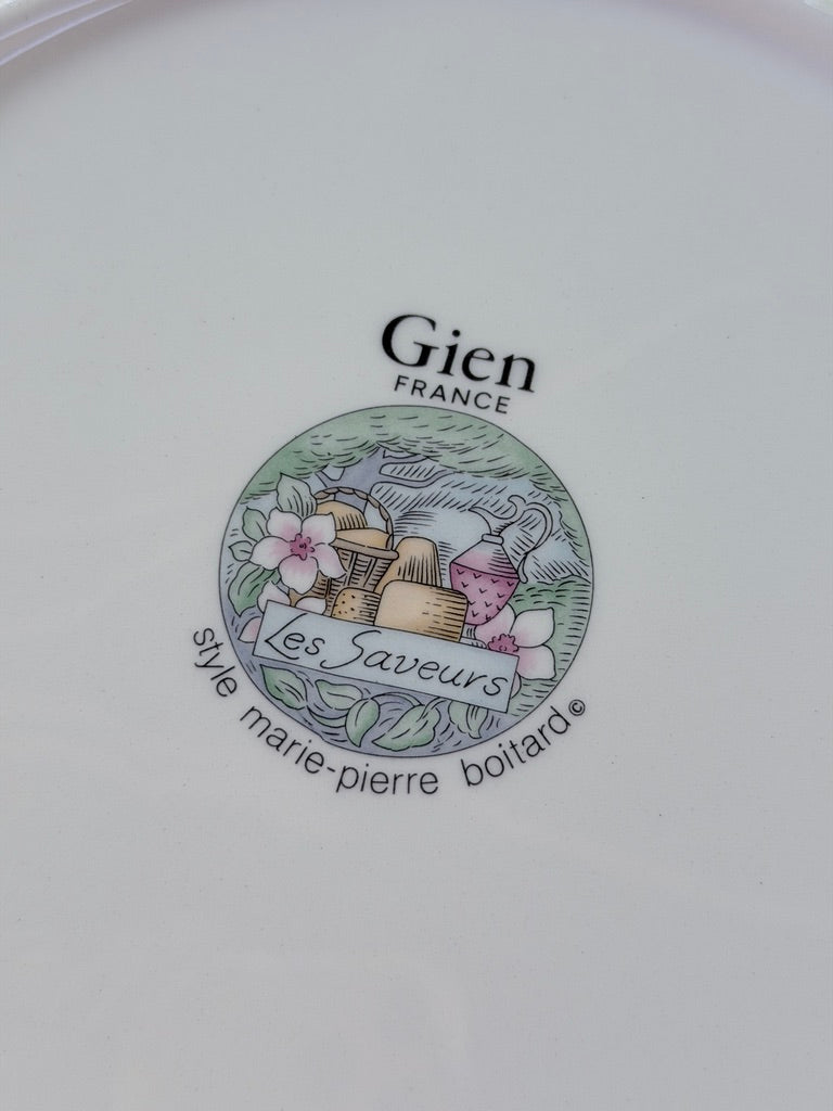 Close-up of a white ceramic plate featuring a circular Gien France logo with the text 'Les Saveurs' and 'syne marie-pierre boittard'.
